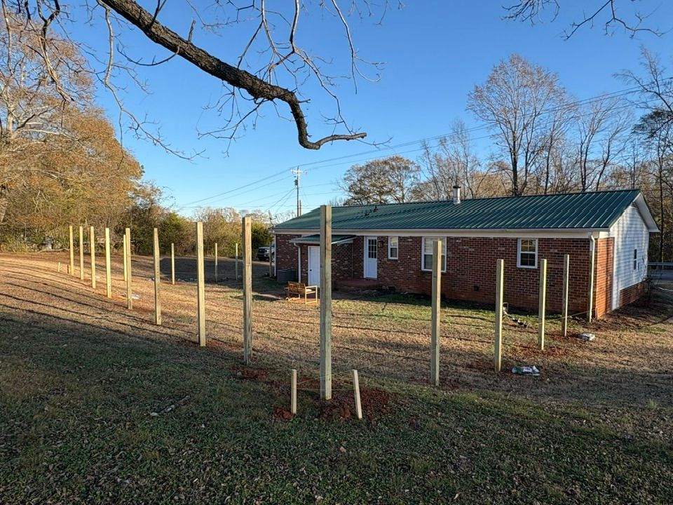 Brick house beside fenced yard with newly installed wooden posts and a tree in front