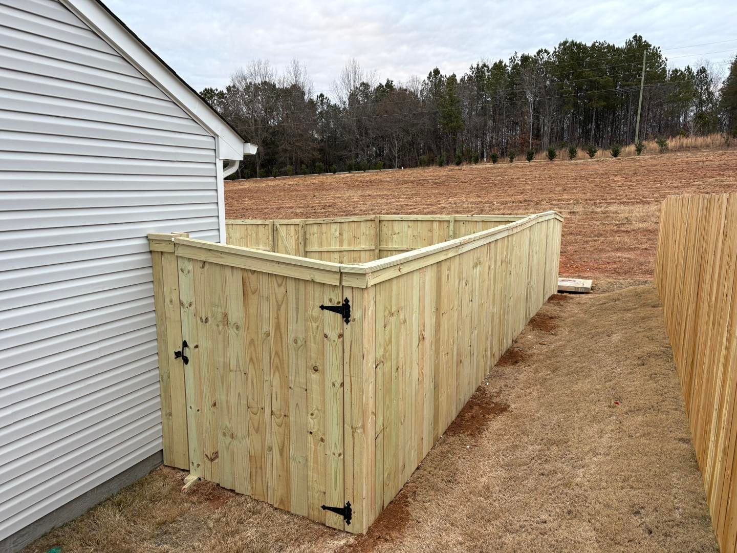 Wooden fenced enclosure beside a house in a grassy field