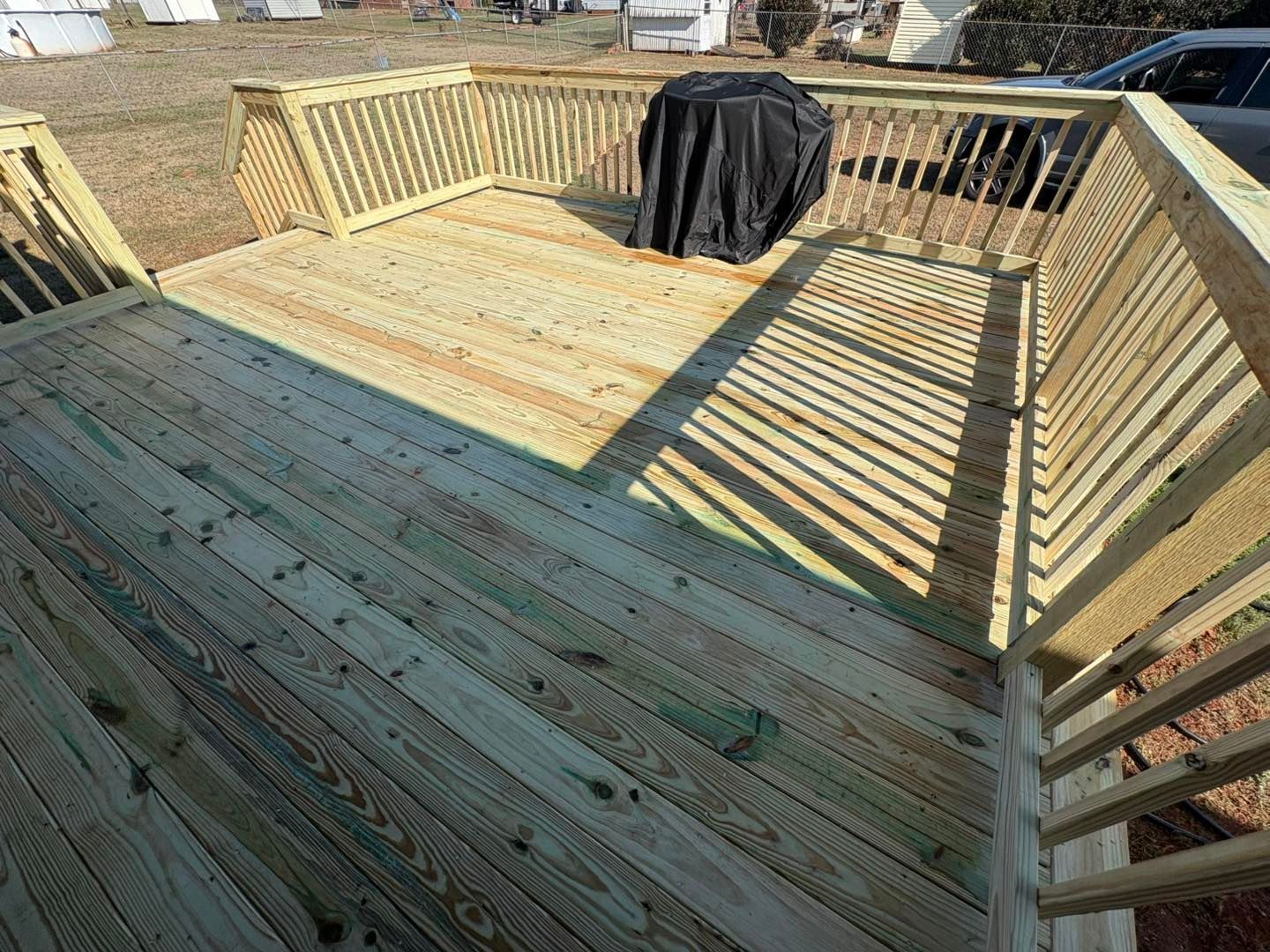 Wooden deck frame with railings and a black grill cover in the center, viewed from above