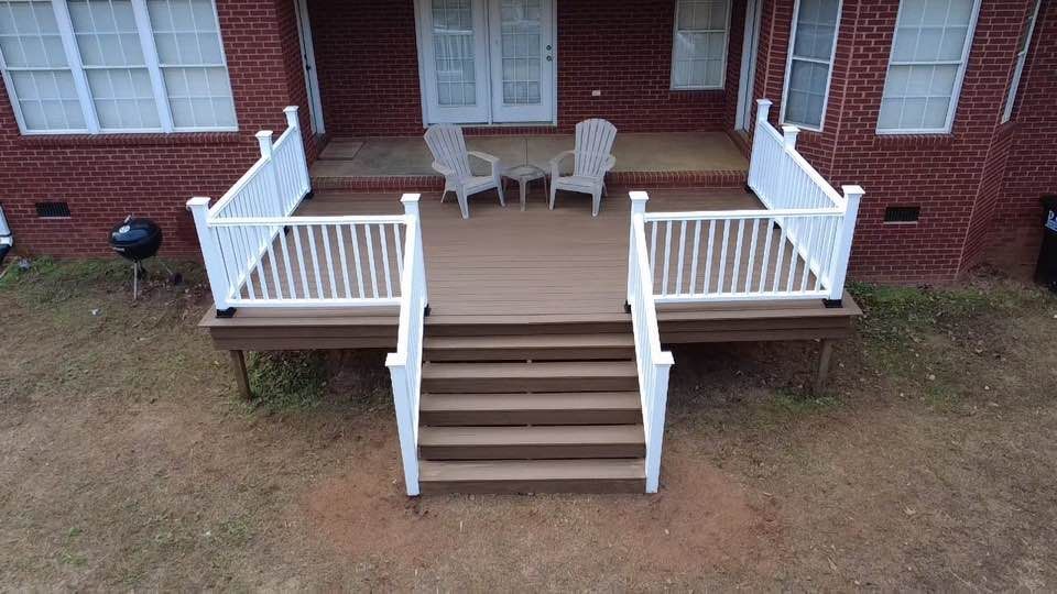 Brick house back porch with white railing, wooden steps, and two patio chairs.
