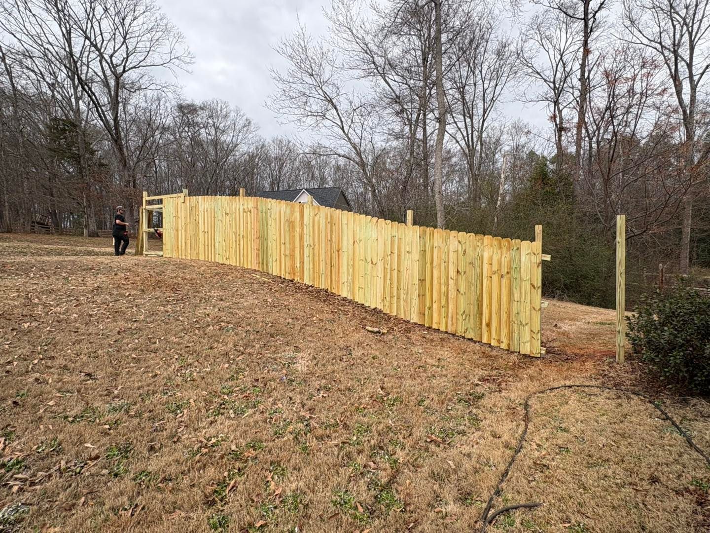 Wooden privacy fence under construction on a wooded hillside with two workers nearby