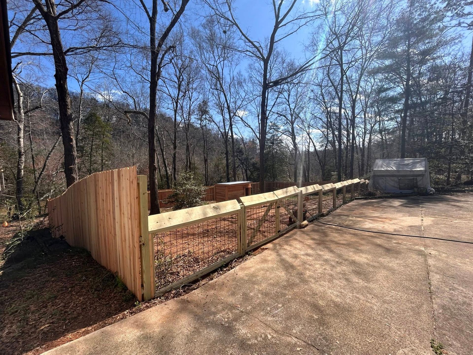Wooden retaining wall and fence beside a paved driveway in a wooded area