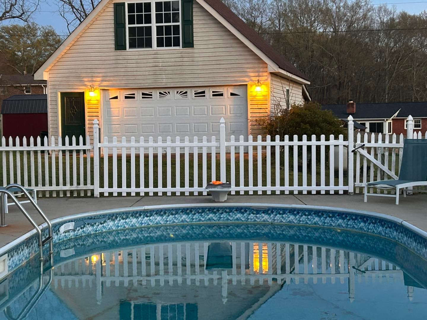 Backyard with above-ground pool, white fence, and a house lit by warm porch lights