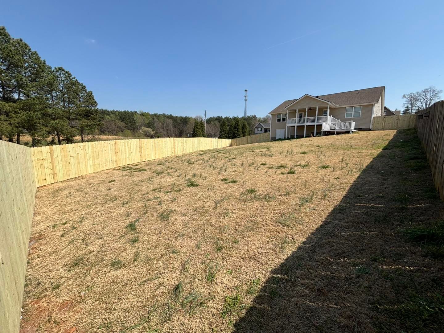 Grassy backyard slope with wooden fence and a house at the top under a clear blue sky