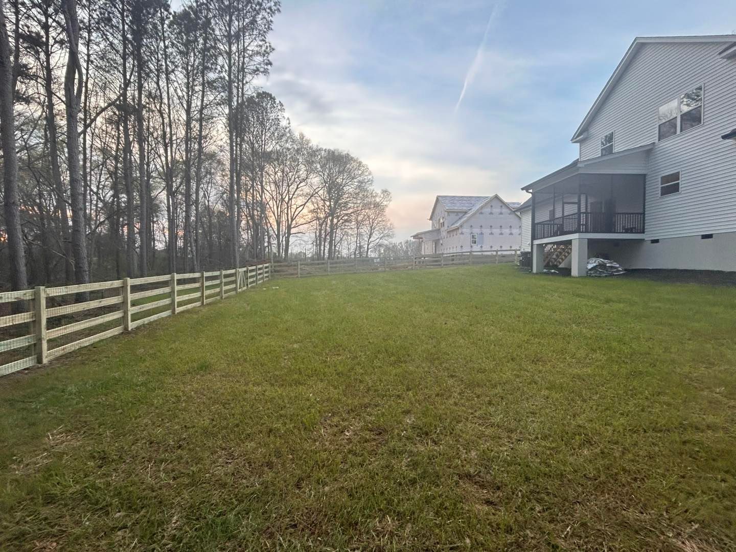 Grassy fenced backyard beside suburban homes at sunset, with trees lining the left side