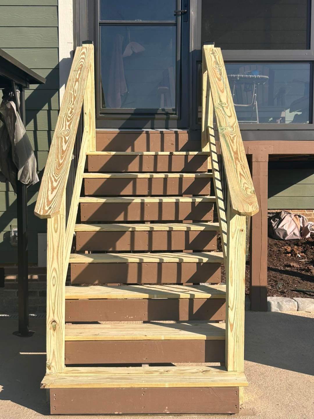 Wooden front steps with railings leading to a house entrance in daylight.
