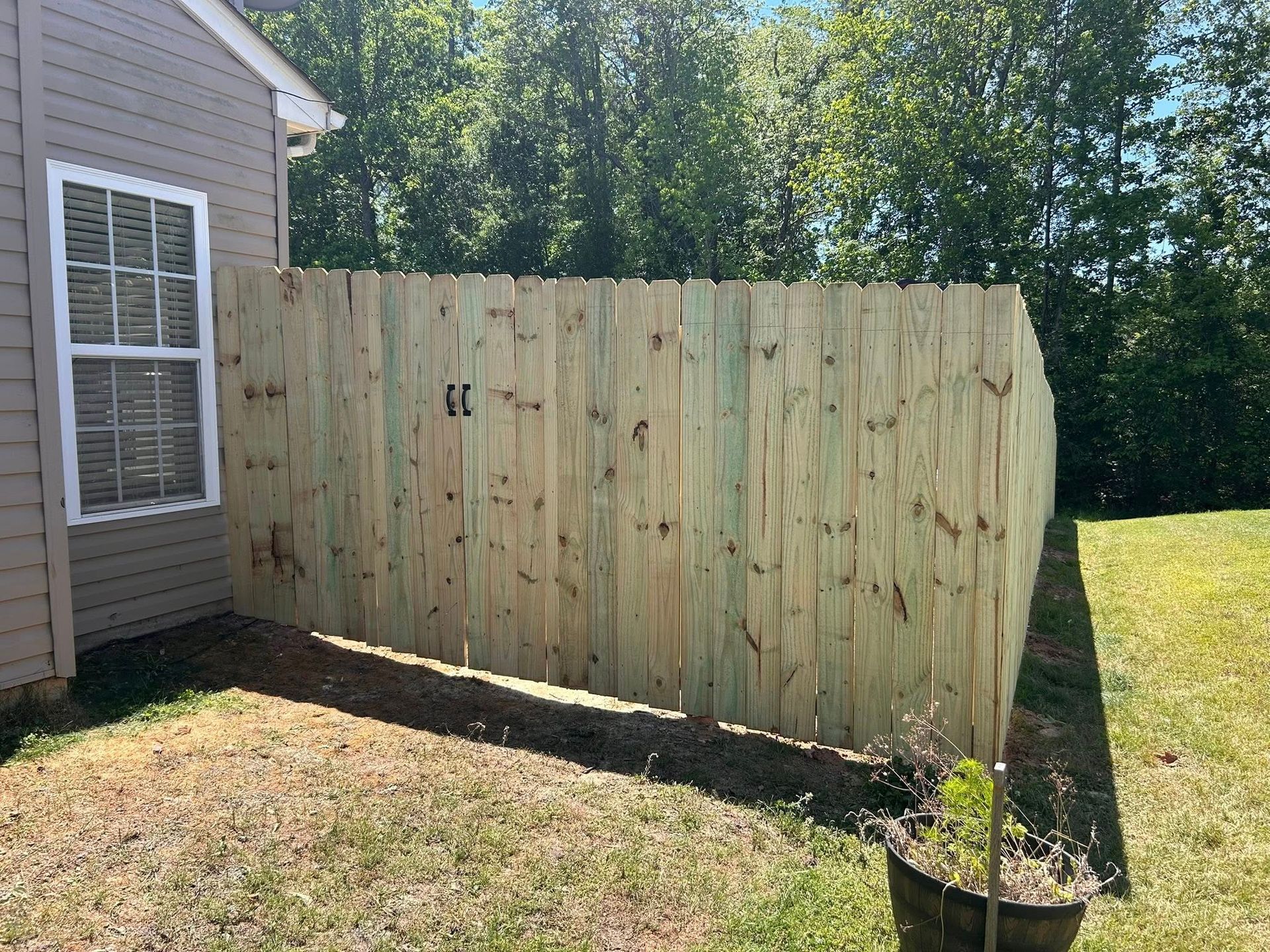 Wooden privacy fence beside a house, with a small gate and slanted fence panel in a sunny yard