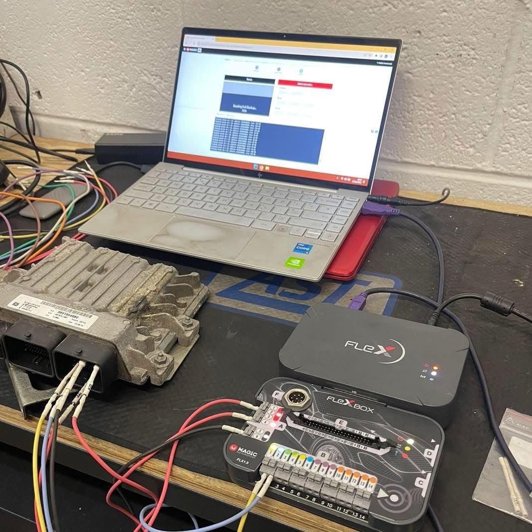 Laptop connected to electronics boards and cables on a workbench, displaying software on screen