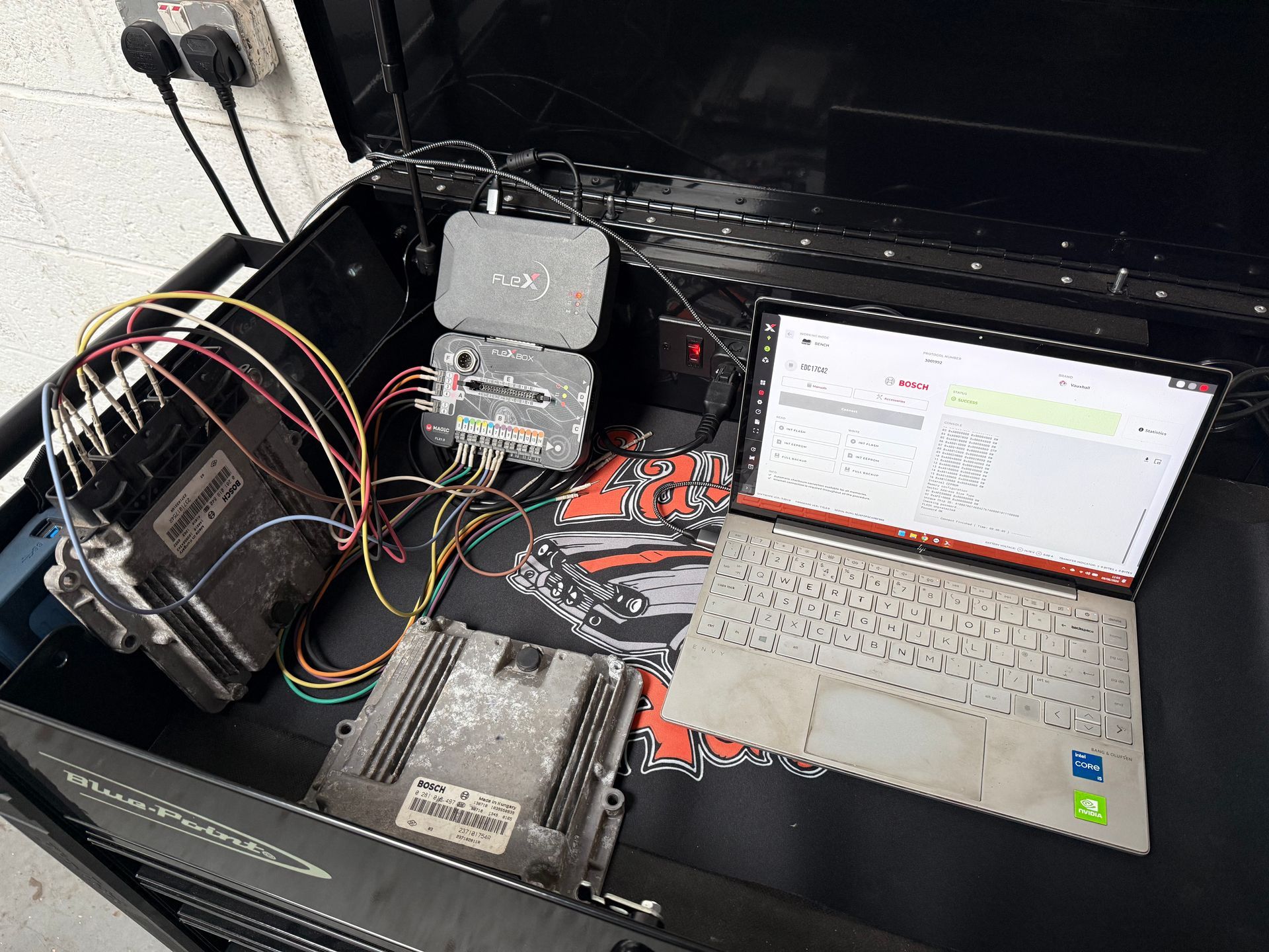 Electronics workbench with wires, circuit boards, and an open laptop displaying code or diagnostics