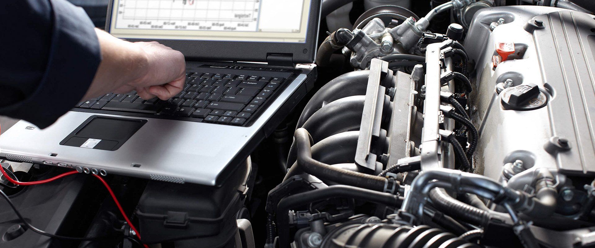 Person using a laptop beside an open car engine in a garage