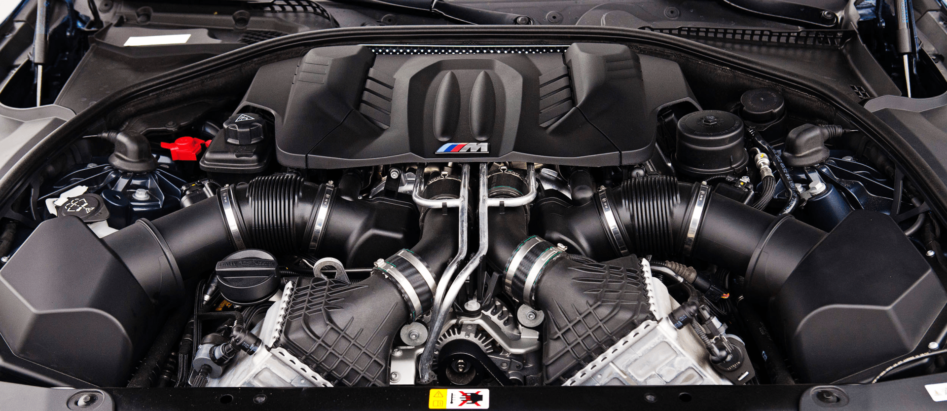 Close-up of a car engine bay with a carbon-fiber intake and black hoses