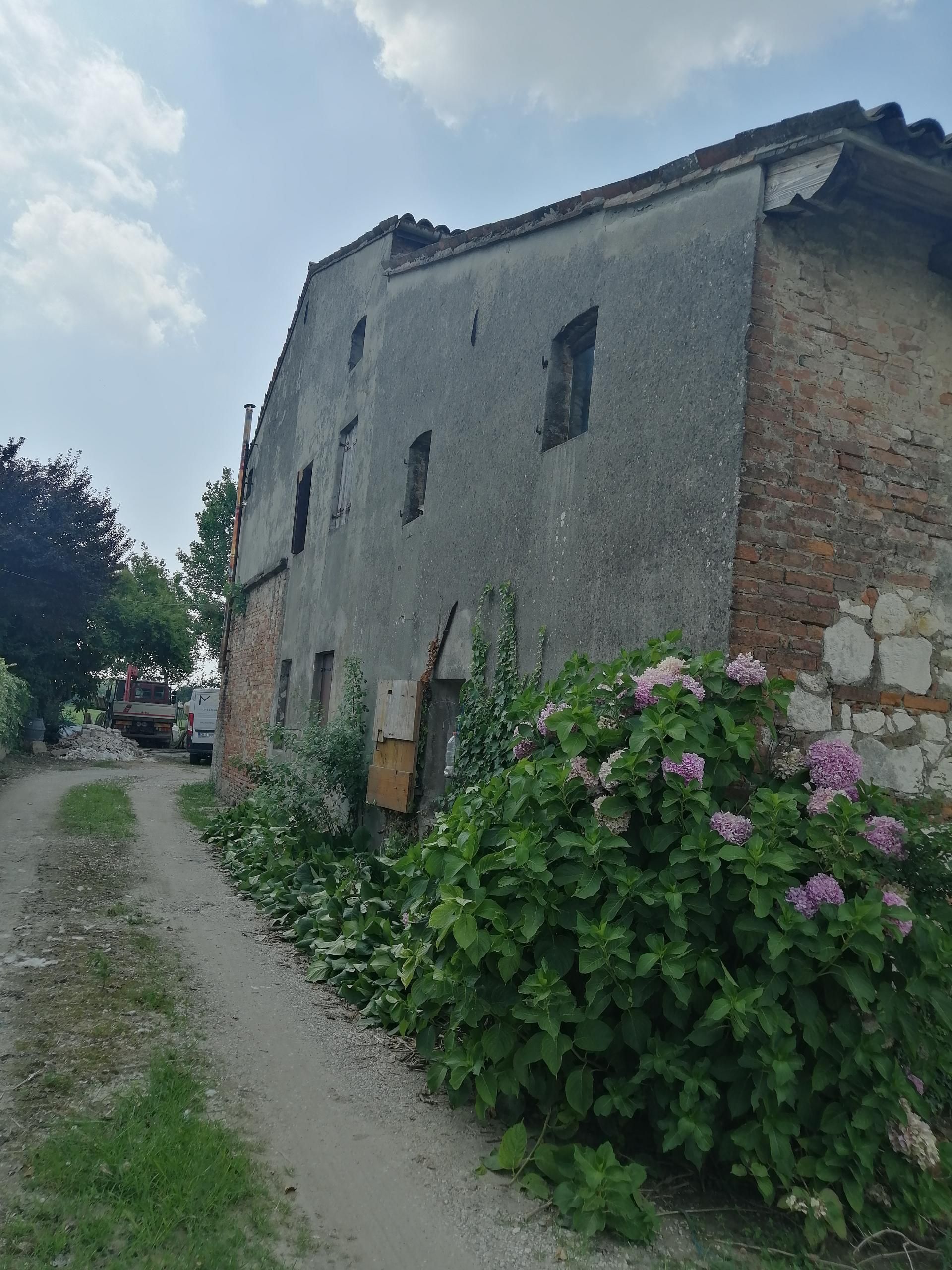 Un edificio in mattoni con dei fiori di fronte e una strada sterrata che conduce ad esso.