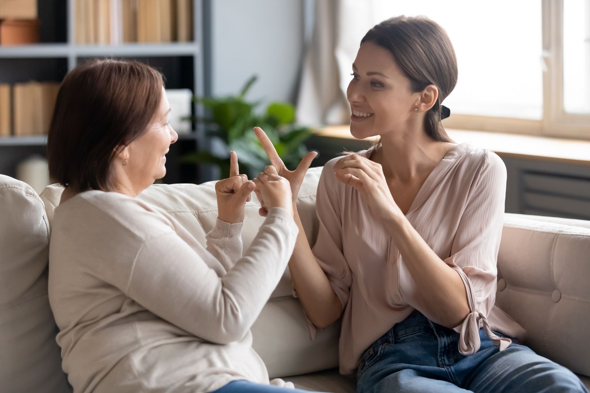 Two women are sitting on a couch talking to each other in sign language.