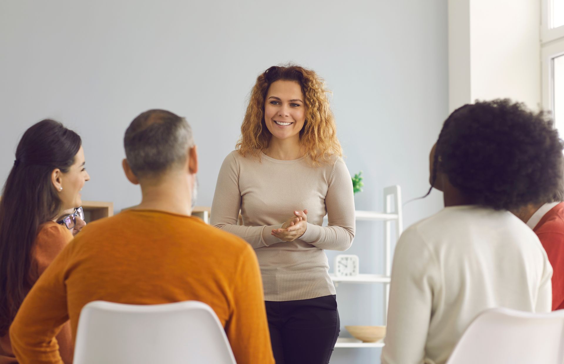 A woman is standing in front of a group of people sitting in chairs.