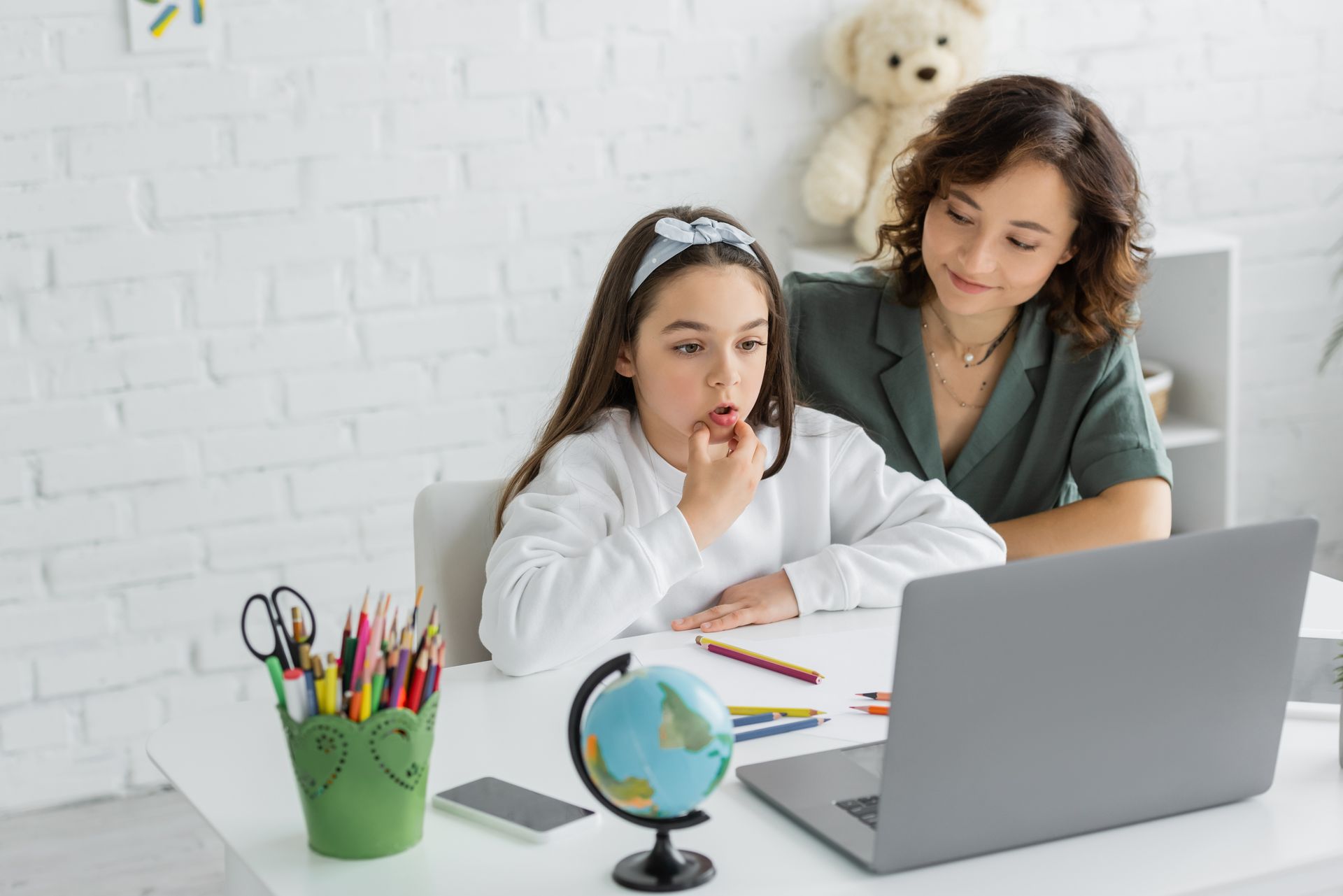 A mother and daughter are sitting at a table looking at a laptop computer.