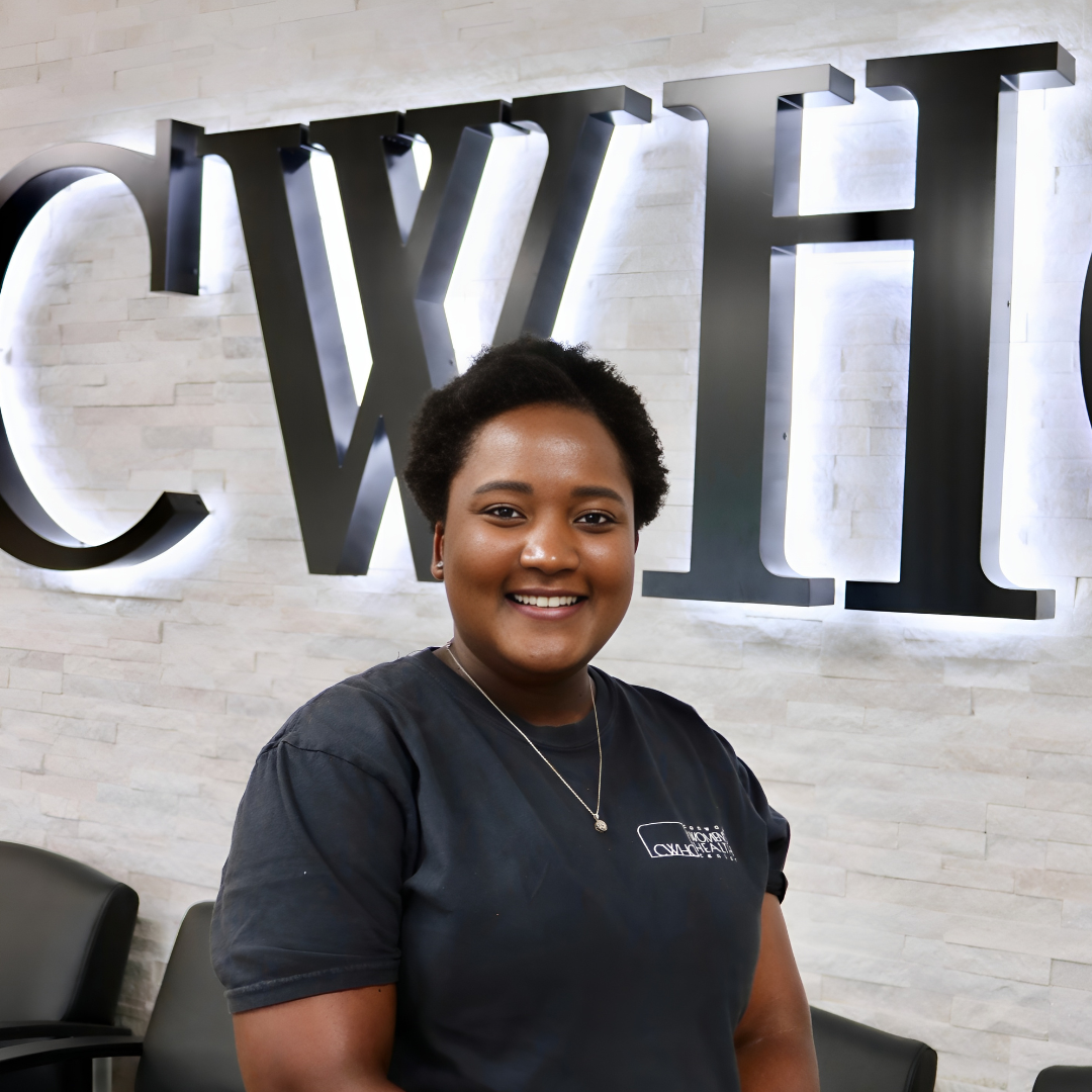 Smiling person in a black shirt standing indoors before a wall with large CWH letters