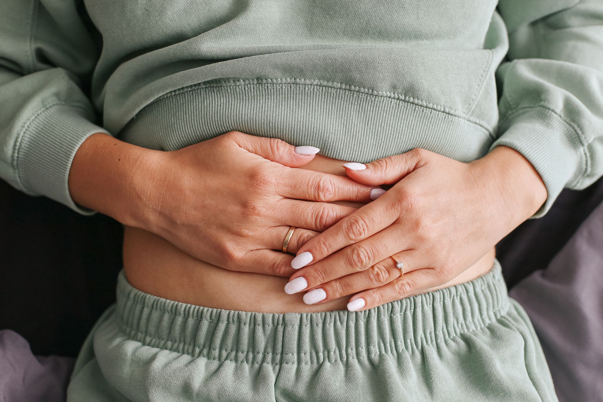 Hands resting over a lower abdomen in a green sweatshirt and pants