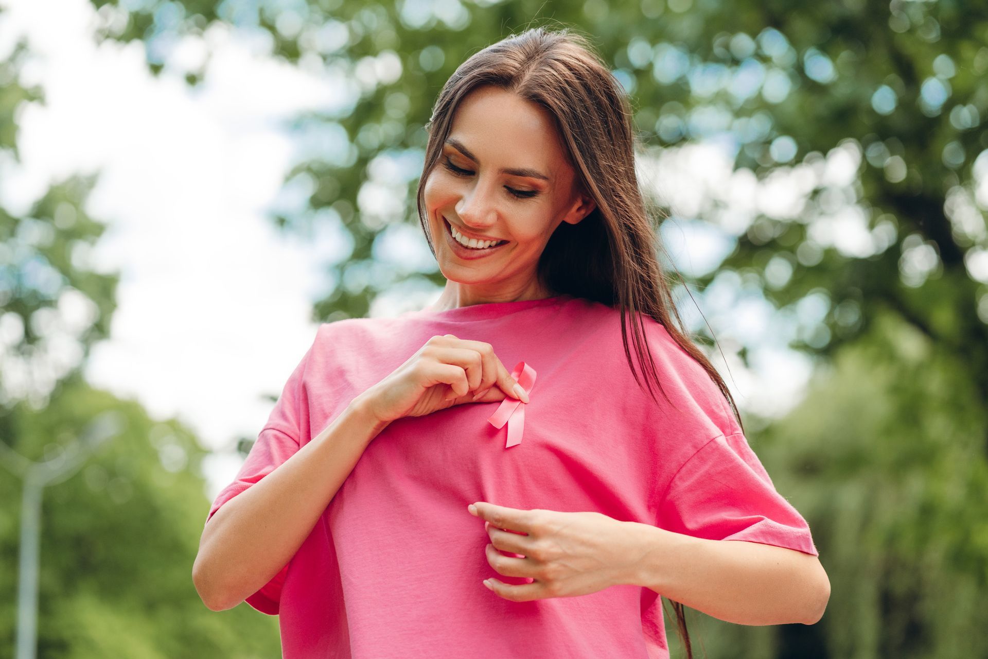 Woman in a pink shirt pinning a pink ribbon on her chest outdoors