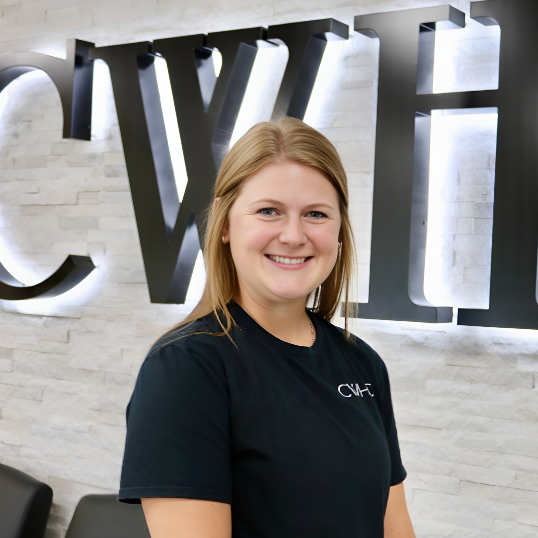 Smiling woman in a black T-shirt standing in front of a lit wall sign