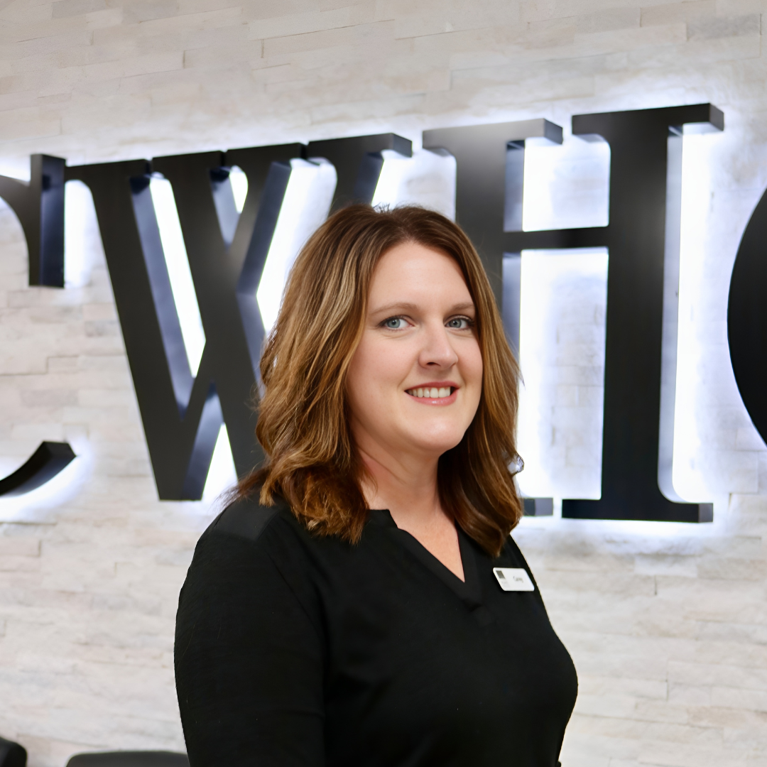 Woman in a black top smiling in front of a wall with large backlit letters
