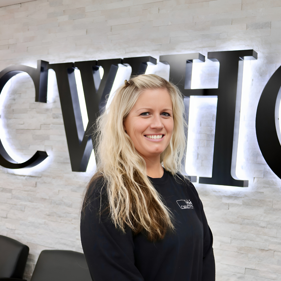 Smiling woman with long blonde hair standing in front of a wall with large black letters