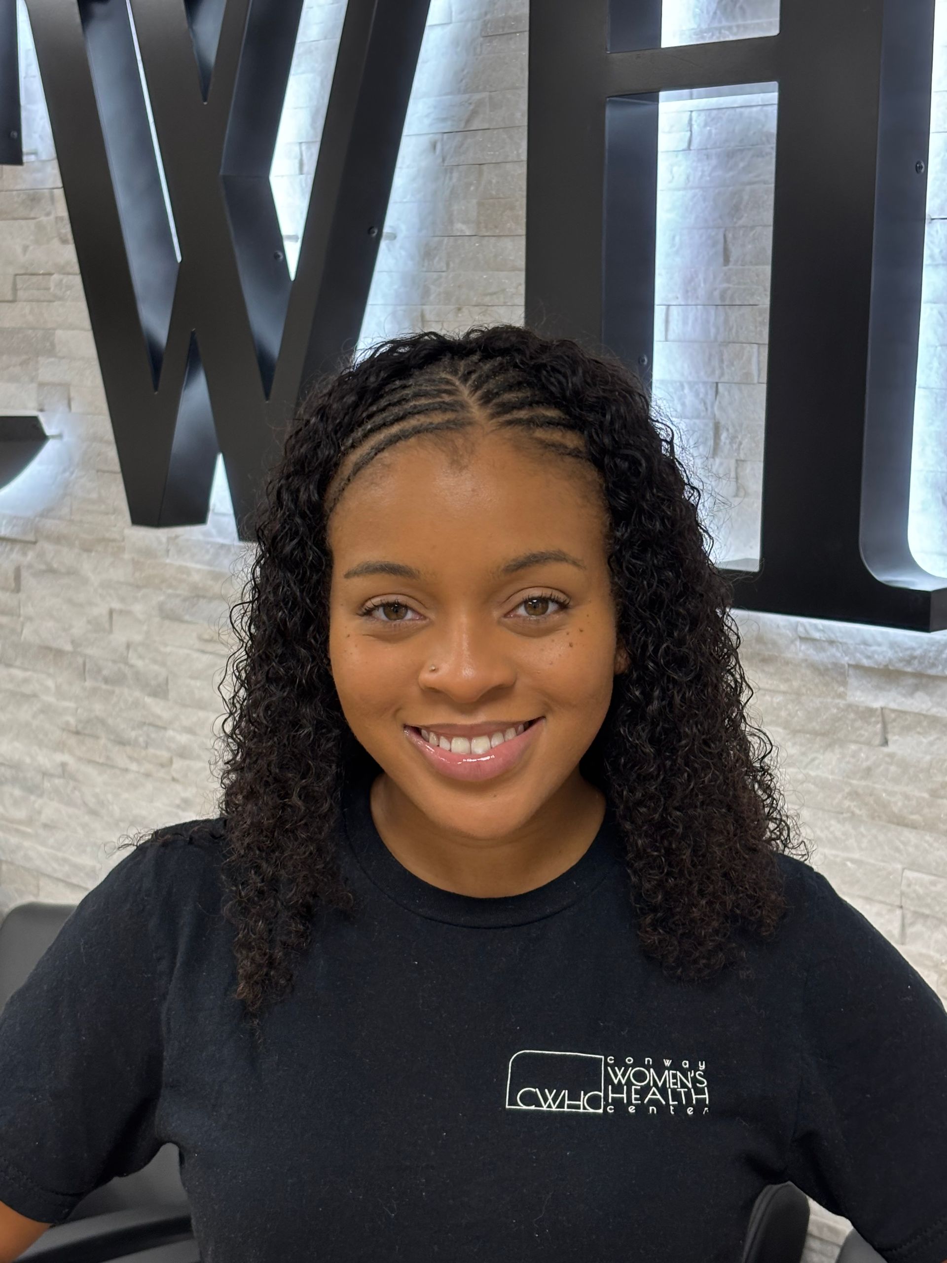 Smiling person in a black shirt standing in front of large black letters on a wall