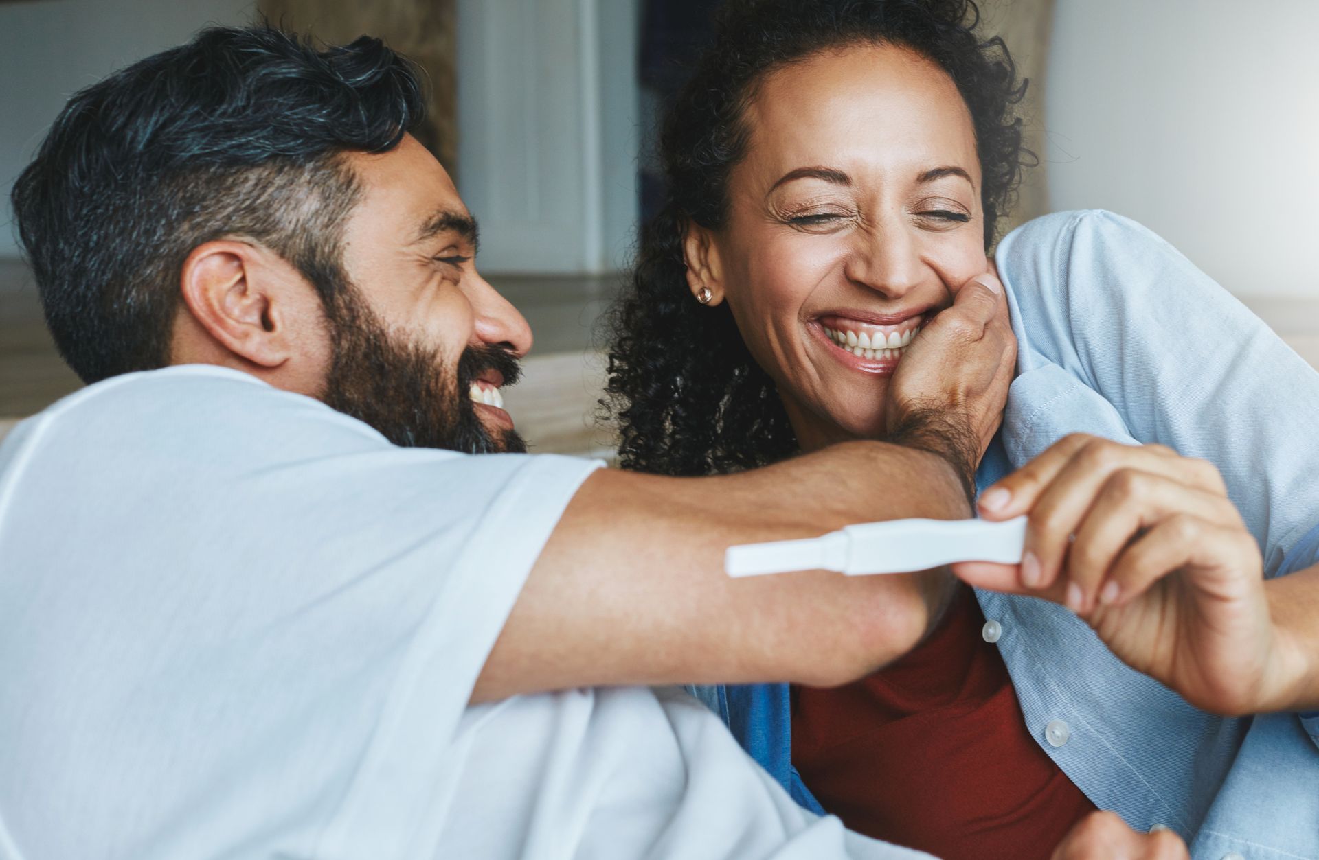 Smiling couple on a couch holding a pregnancy test and laughing together