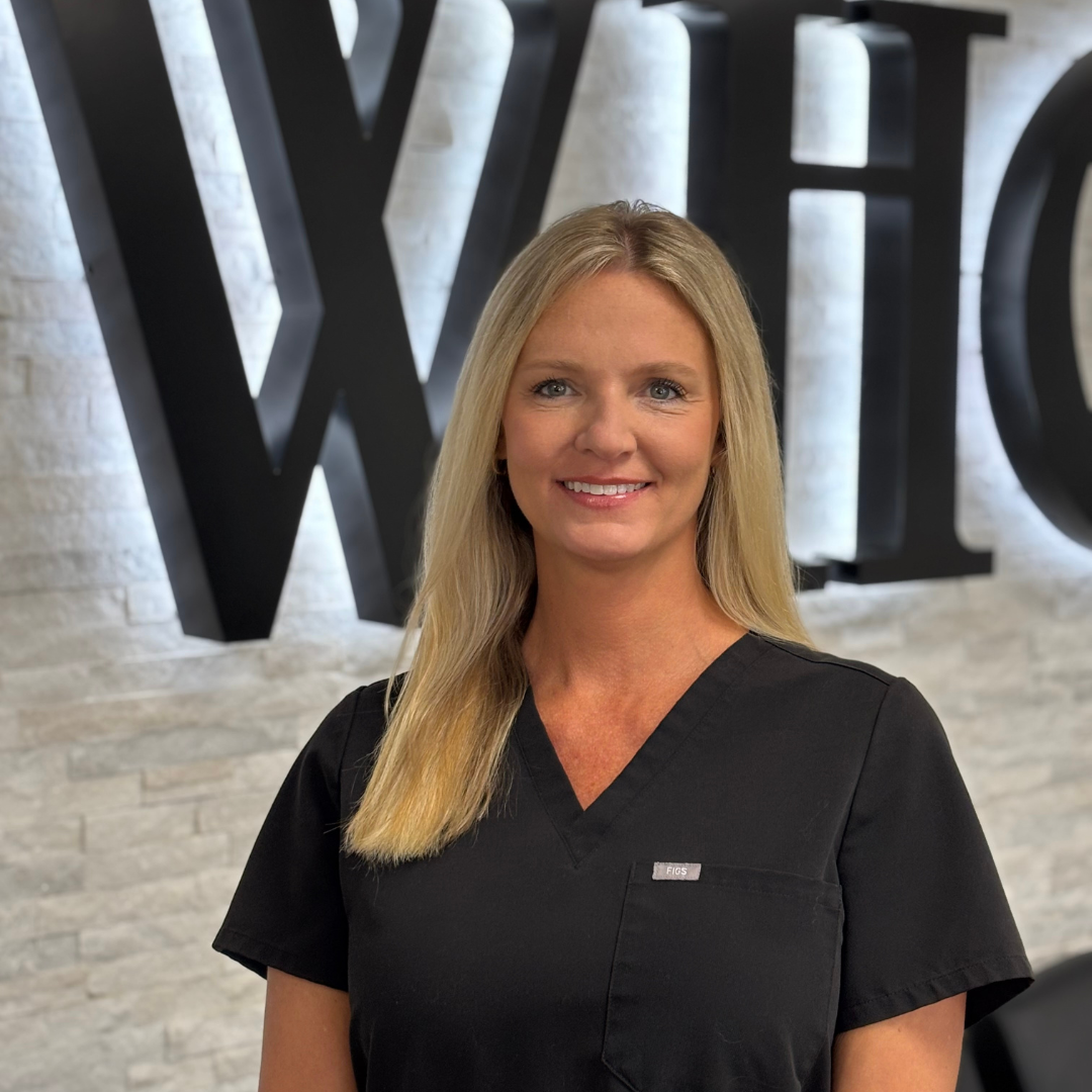 Smiling woman in black scrubs standing before a wall with large letters