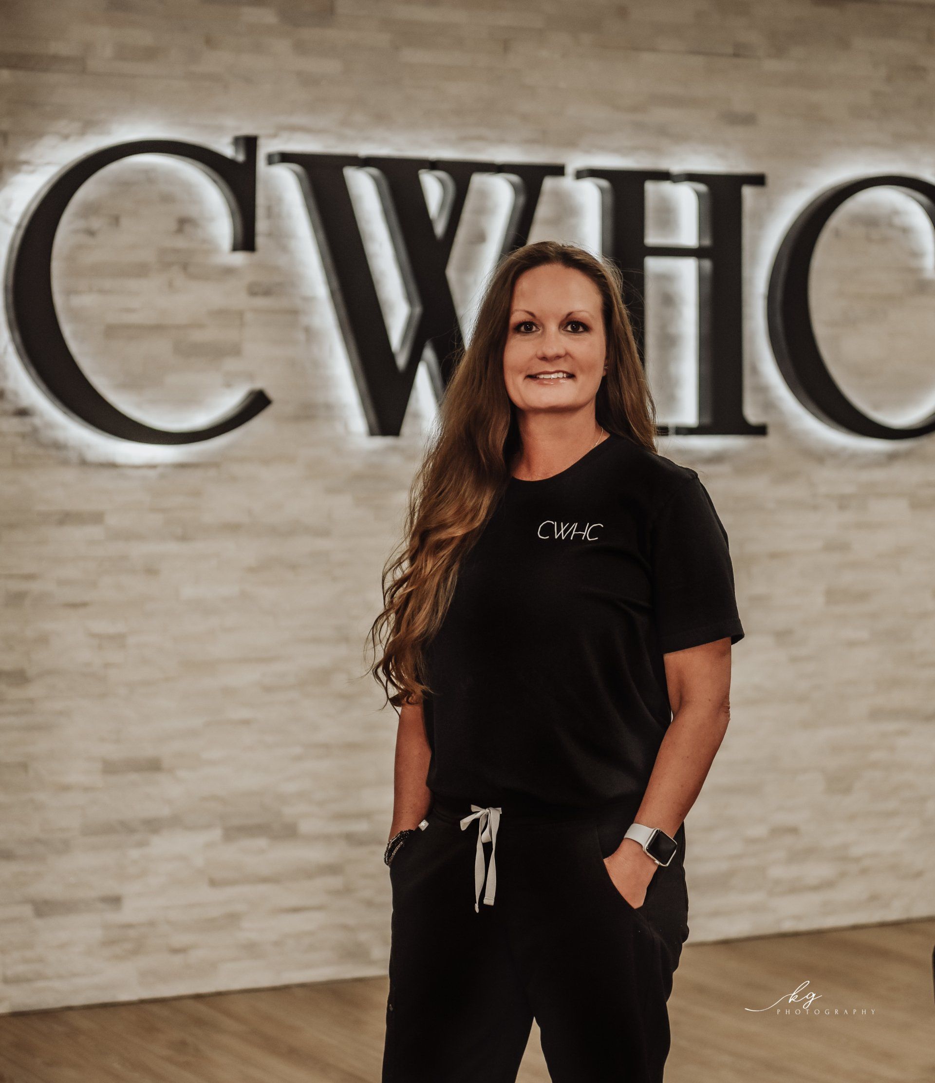 Woman standing in front of a CWHOC sign, wearing black clothes and smiling