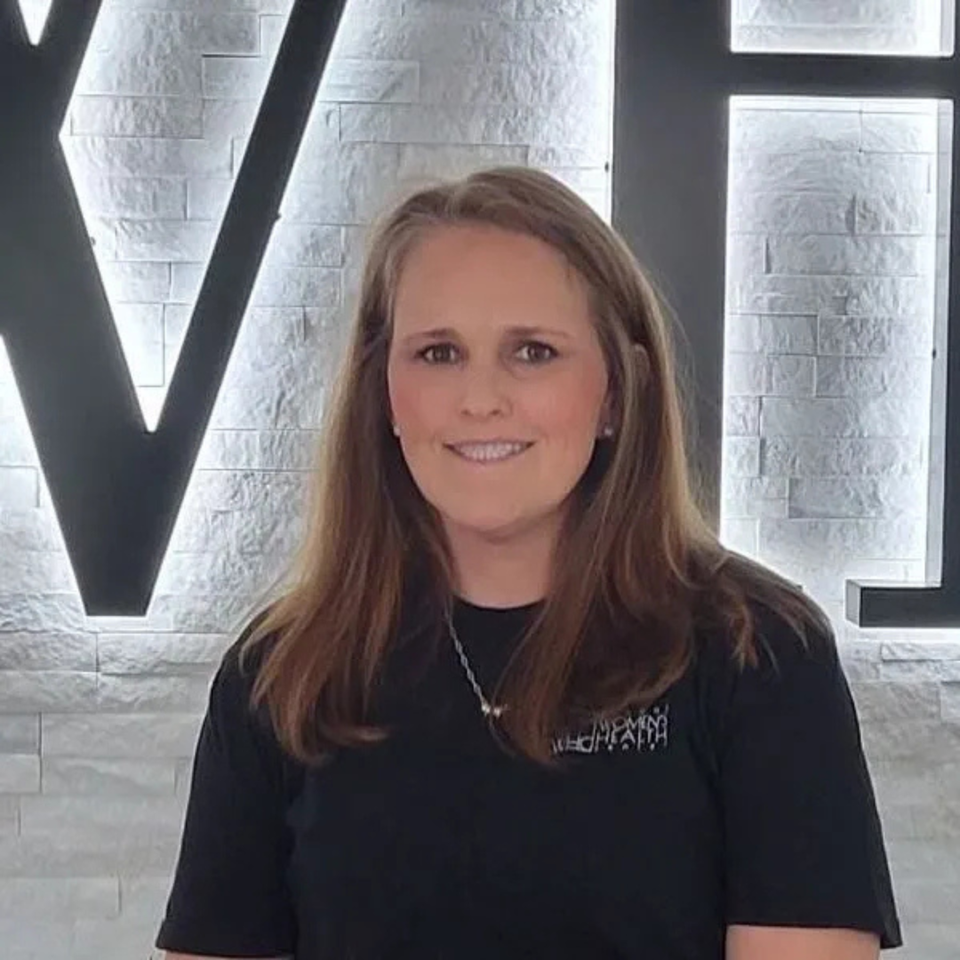 Woman in black shirt standing in front of a lit wall sign with large white letters