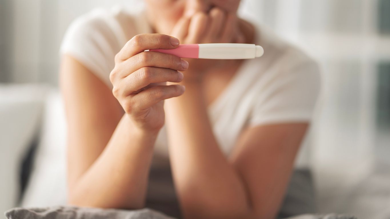 Person holding a pregnancy test with a pink result window in a softly lit room