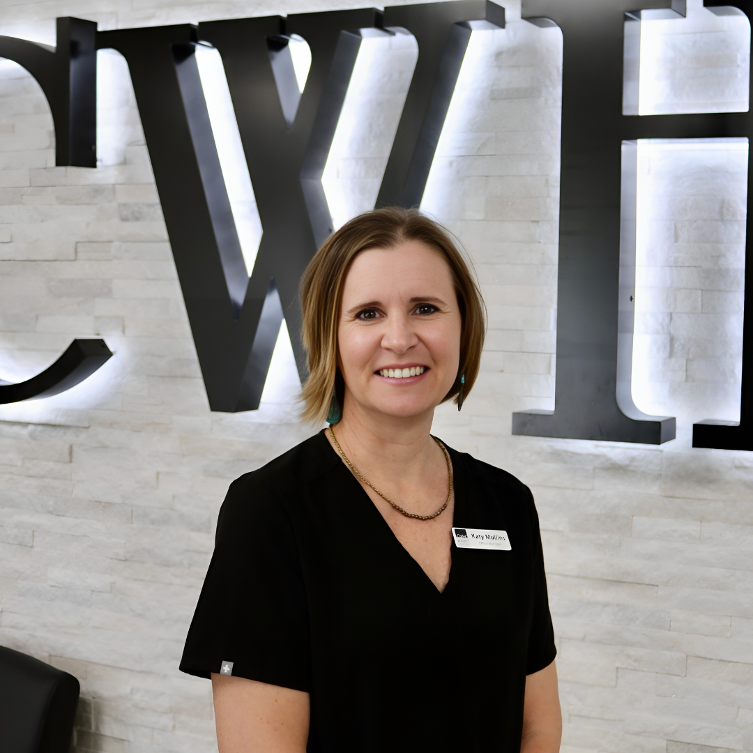 Smiling woman in black blouse standing before large silver letters on a wall