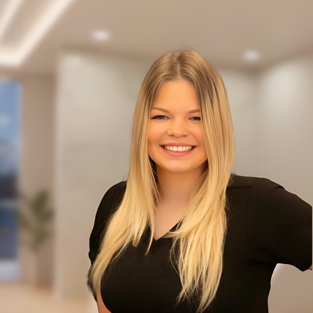 Smiling blonde woman in a black top standing in a blurred indoor office setting