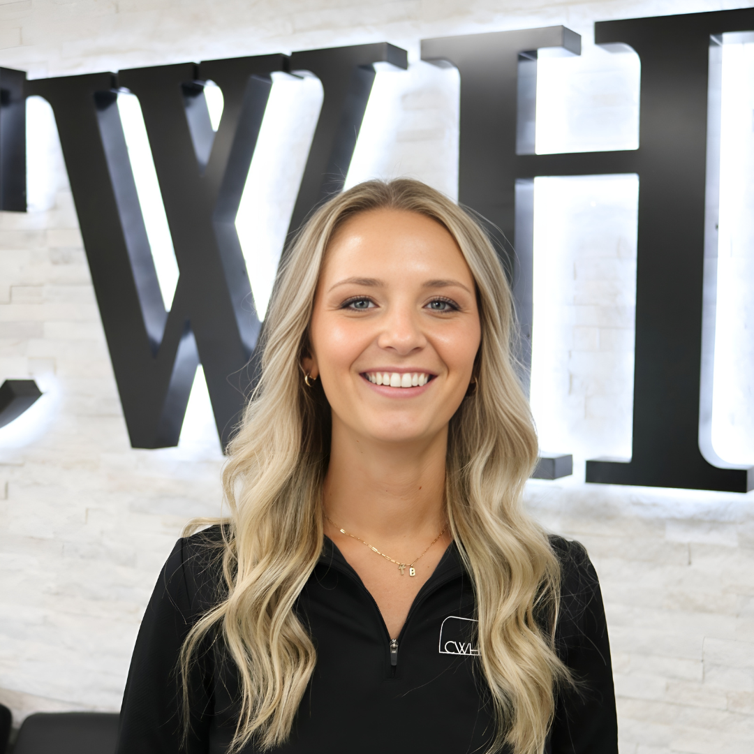 Smiling woman in a black zip-up top standing in front of a large wall sign