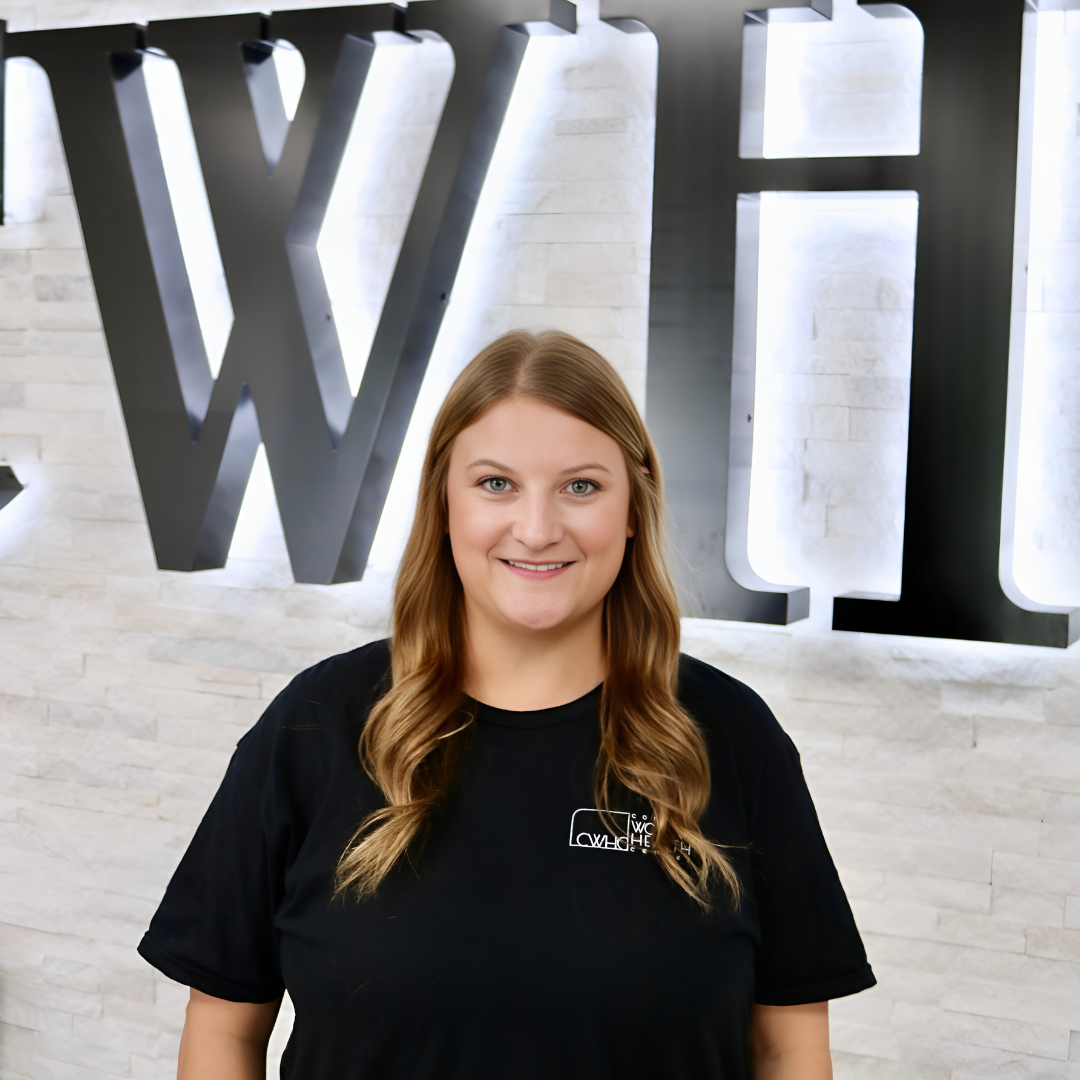 Woman standing in front of a wall with large “WH” letters, smiling at the camera.