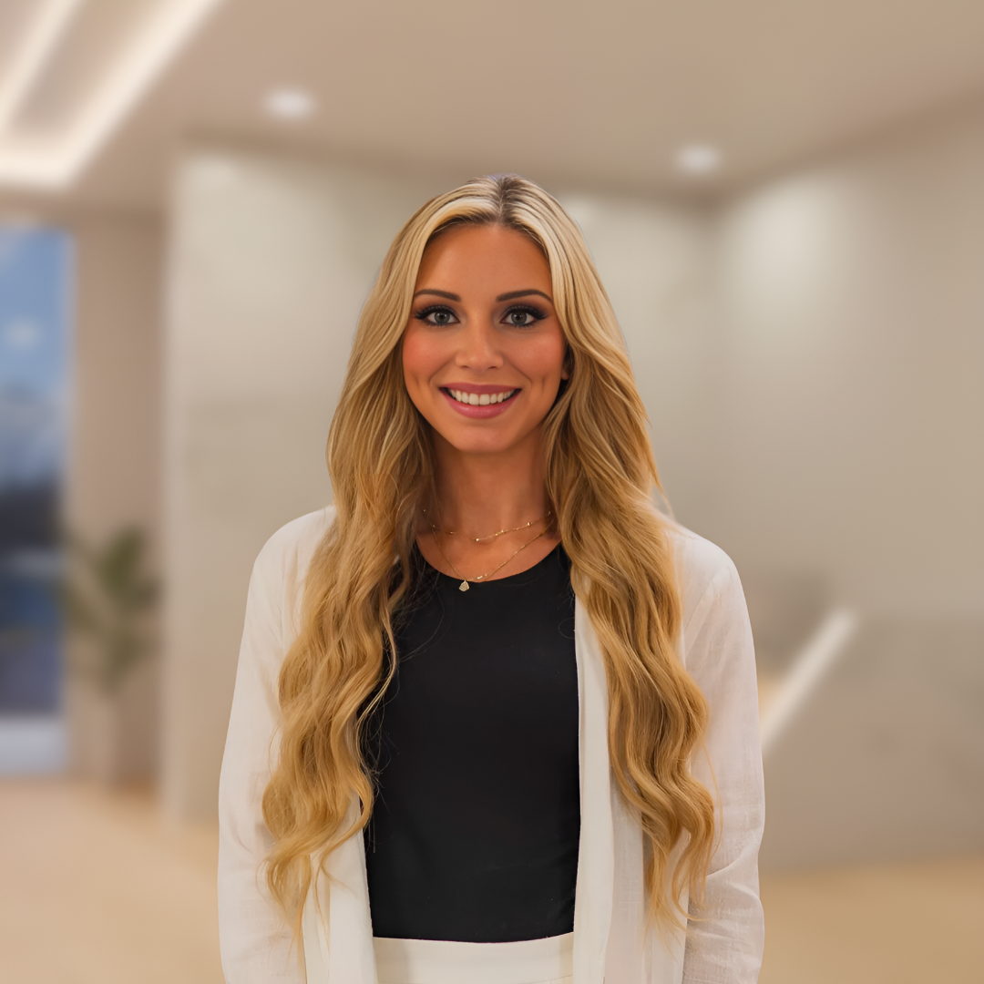 Smiling woman in a black top and white cardigan standing in a softly lit office lobby