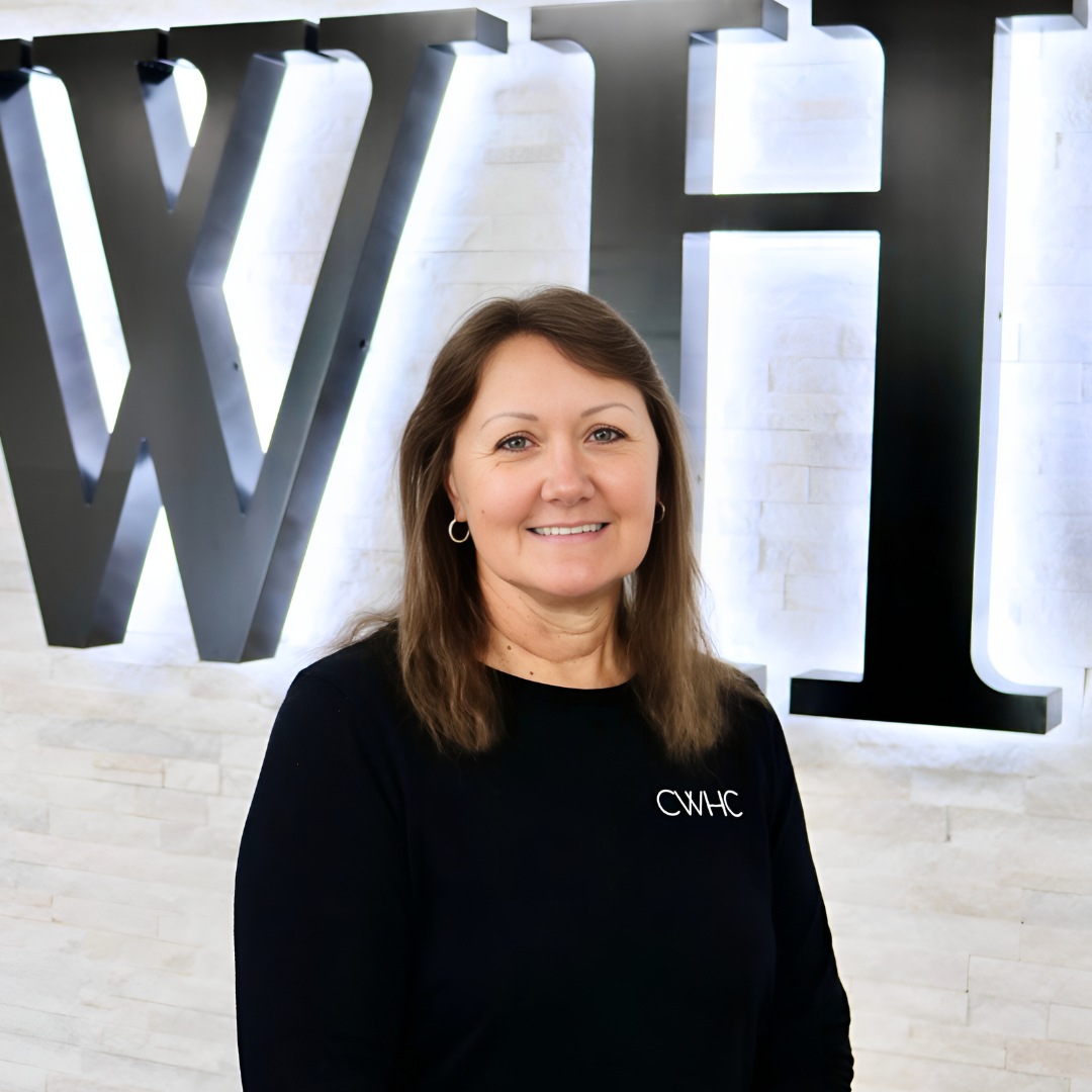 Woman in a black top smiling in front of a large illuminated “WH” sign