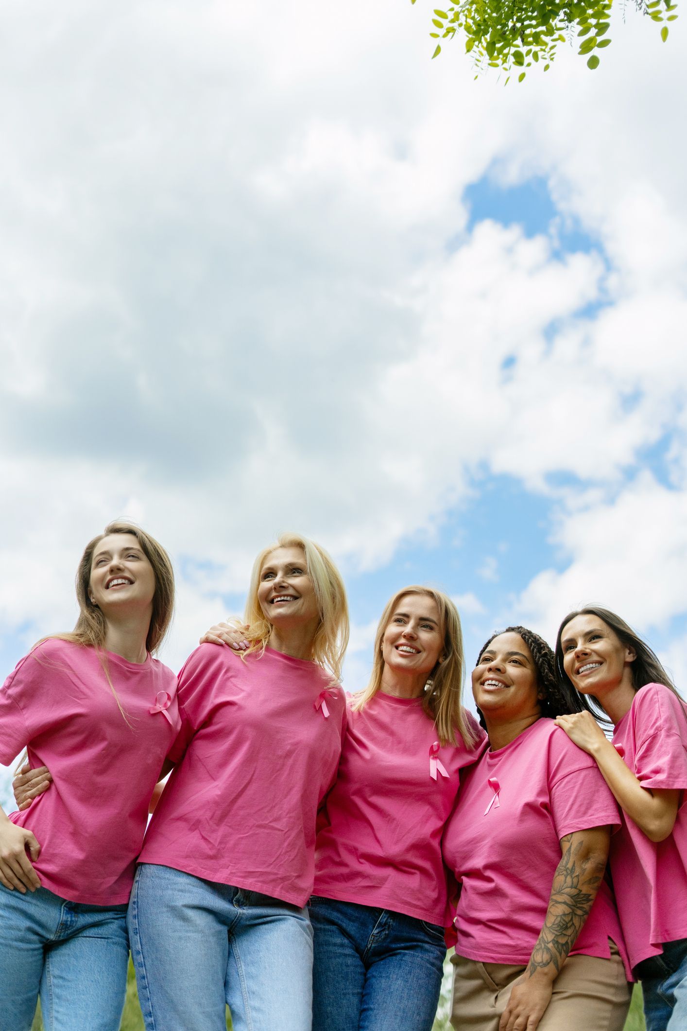 Five people in pink shirts standing together outdoors under a cloudy sky.
