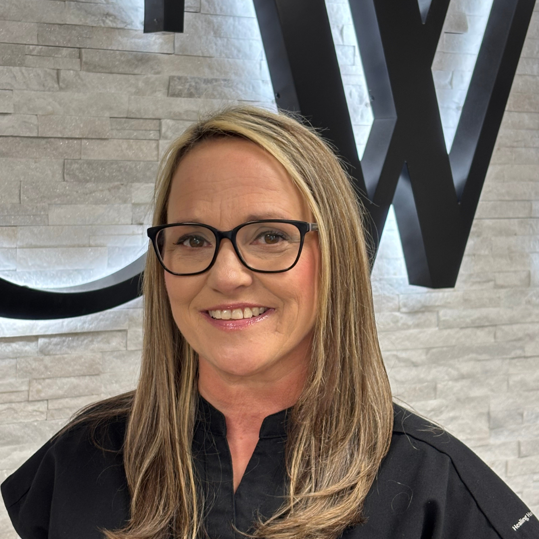 Woman with glasses smiling in front of a stone wall with large black letters
