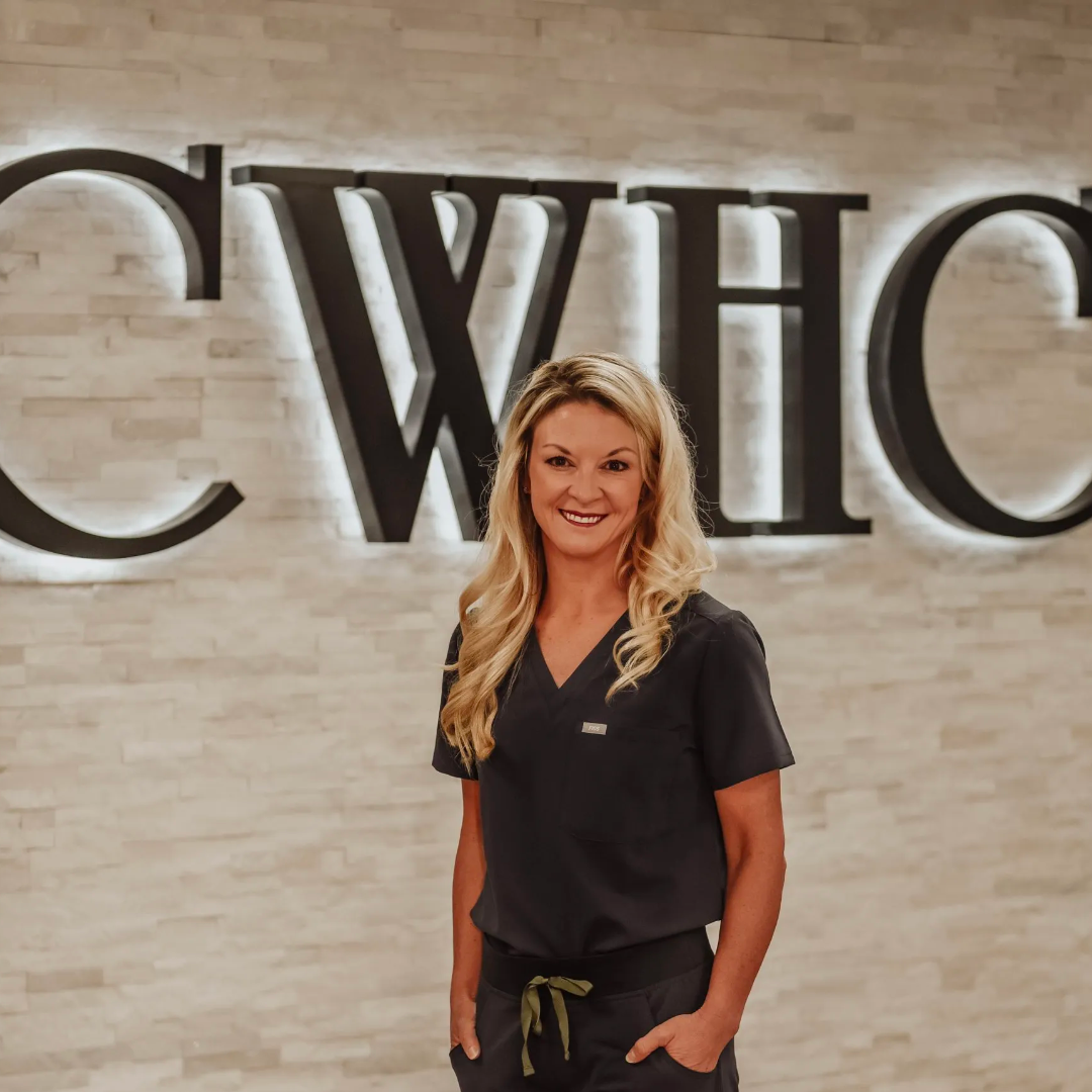 Woman smiling in dark scrubs standing in front of a wall with large illuminated letters