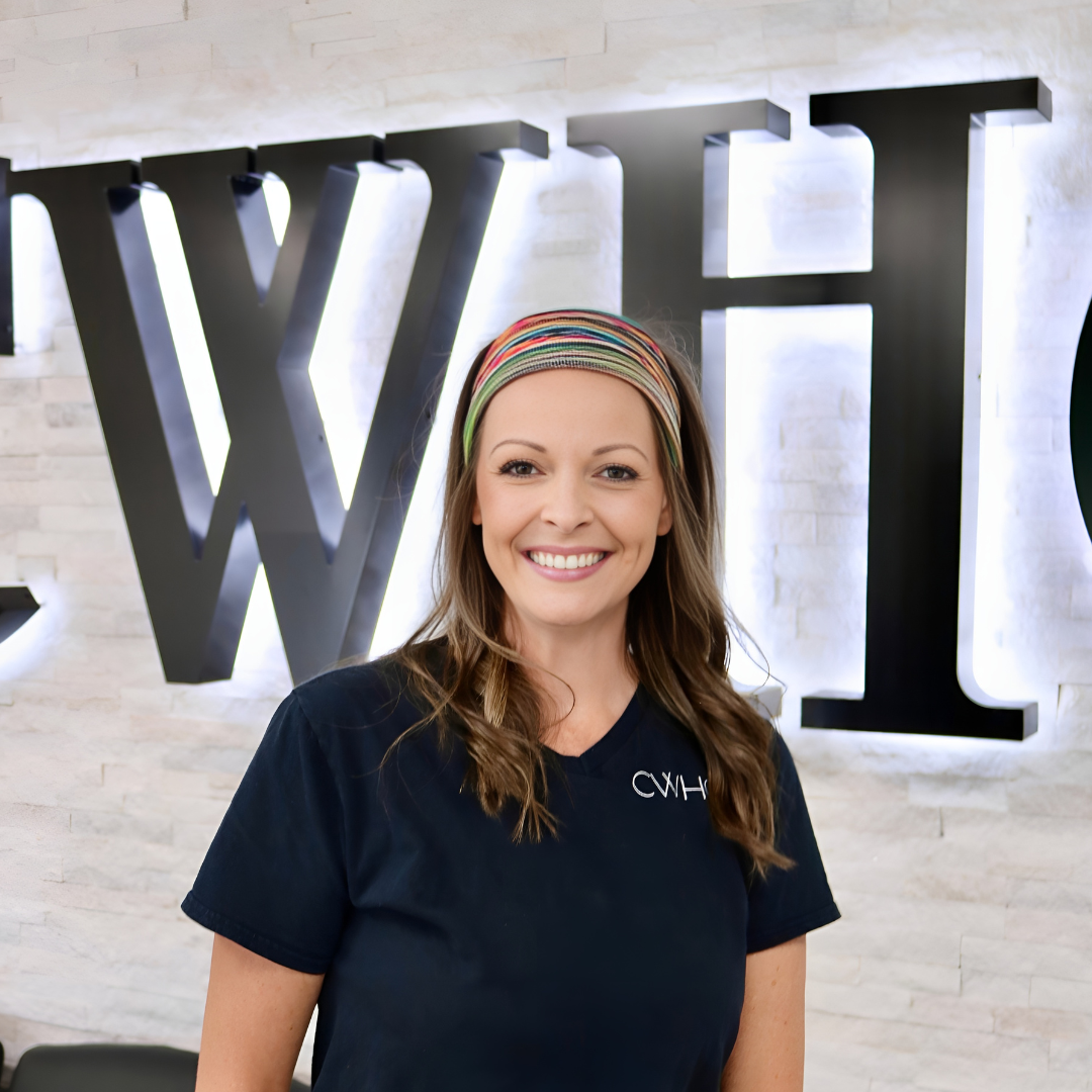Smiling woman in navy shirt standing before large wall letters spelling “WH”