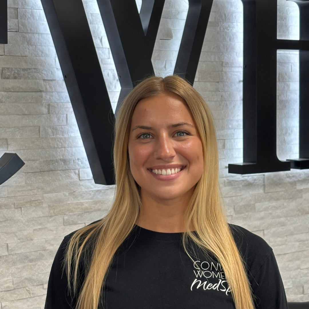 Smiling woman in a black shirt standing before a white brick wall with large black letters