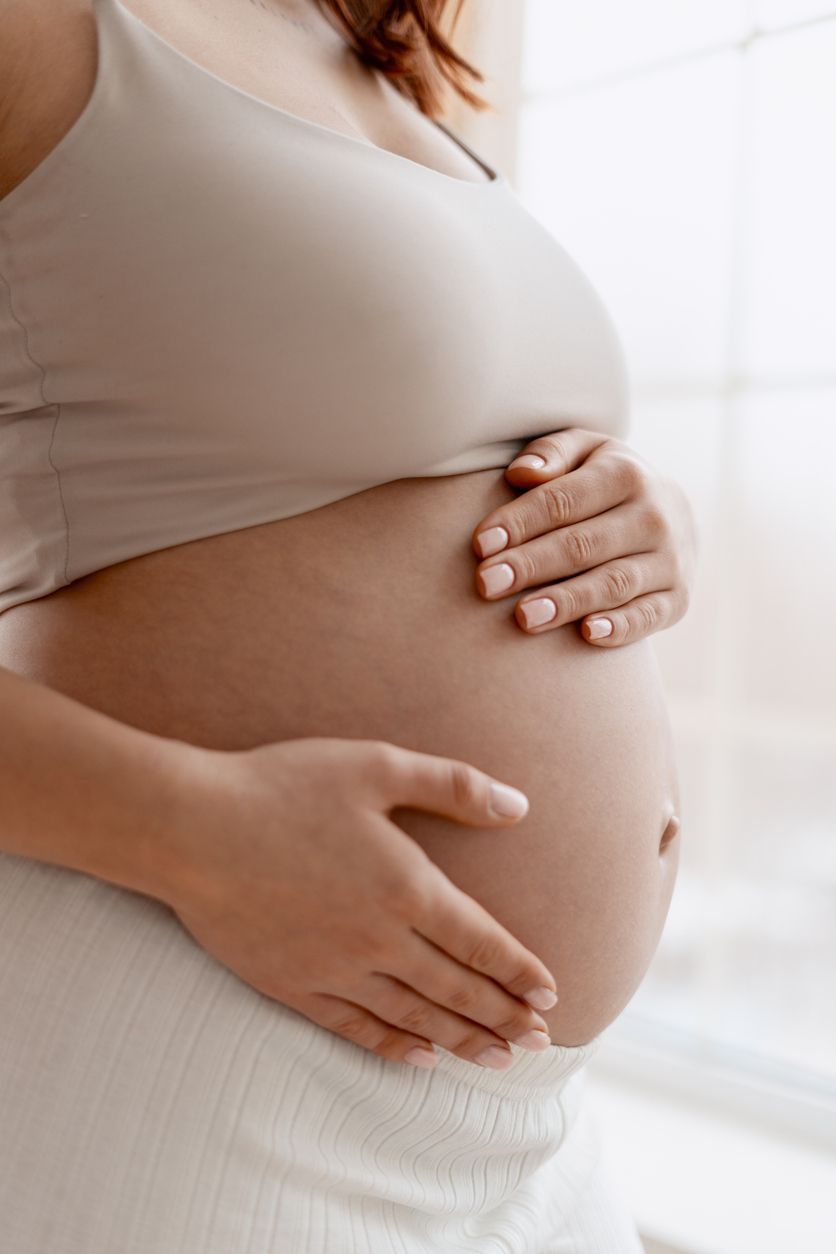 Pregnant person gently holding belly near a bright window