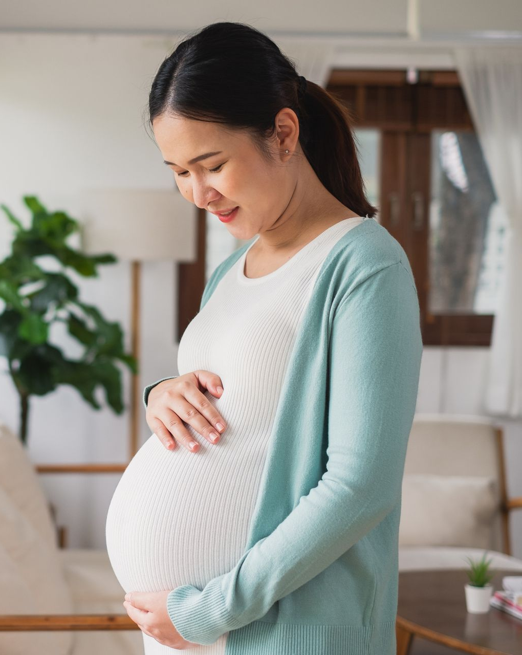 Three pregnant people in pastel outfits posing closely together against a beige background