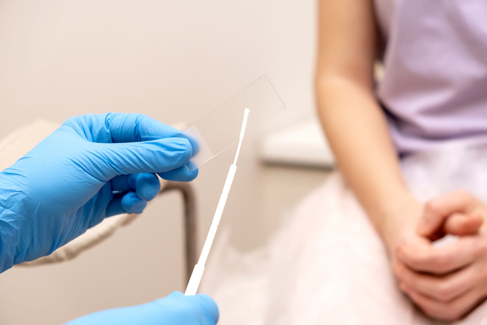 Gloved hand holding a swab near a seated person in a clinical setting