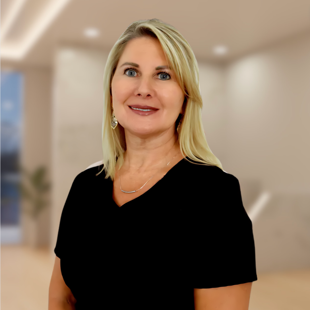 Portrait of a smiling blonde woman in a black top, standing in a softly blurred office hallway