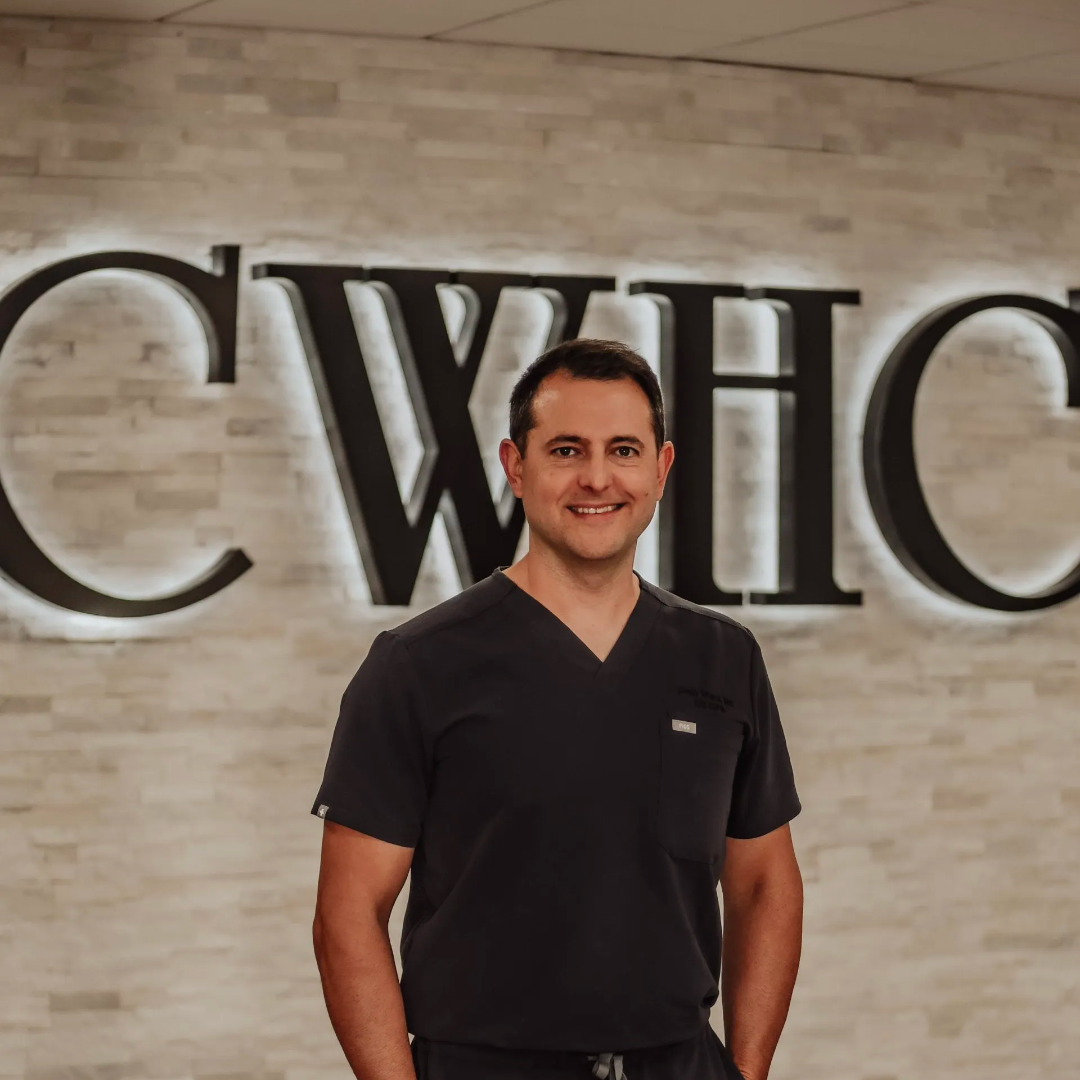 Smiling man in black scrubs standing in front of a CWHC sign in a lobby