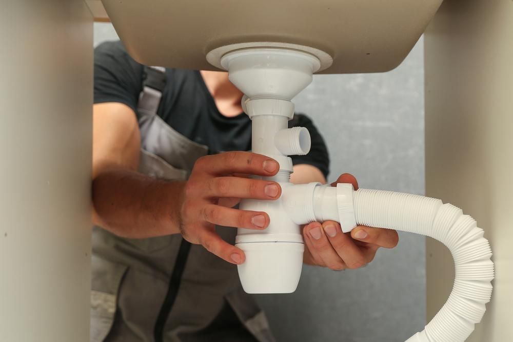 A Plumber Fixing a Pipe Underneath the Sink — Aqua Blue Plumbing Services in Nambucca Heads, NSW