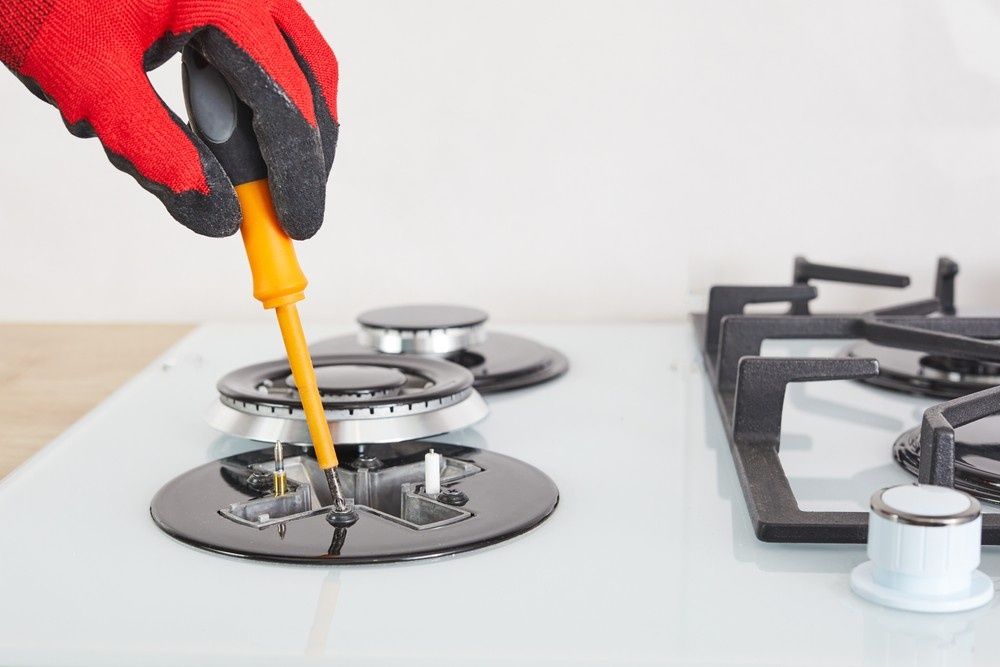 A Man Holding a Screw Fixing a Stove — Aqua Blue Plumbing Services in Coffs Harbour, NSW 