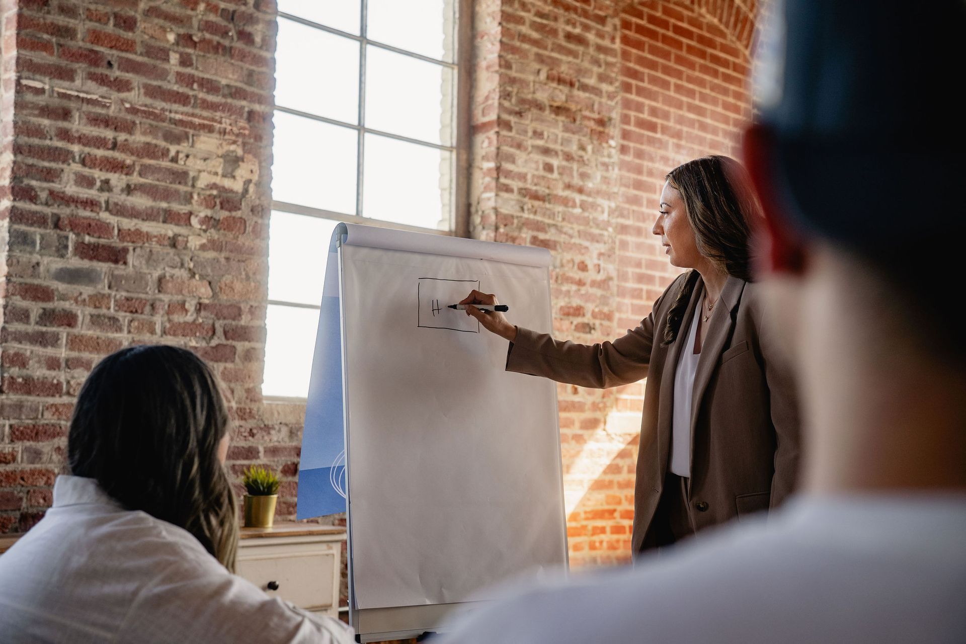 Person presenting at flip chart in a brick-walled meeting room, with attendees listening.